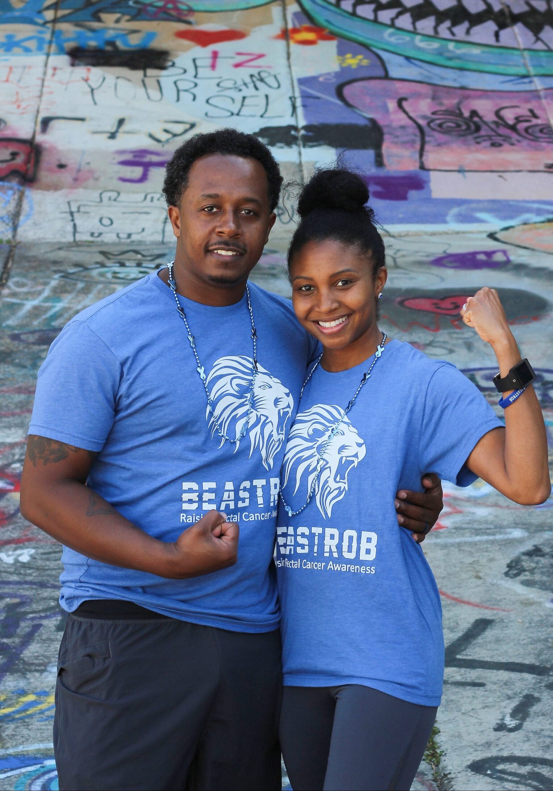 black male and black female in light blue shirt, in front of graffiti wall